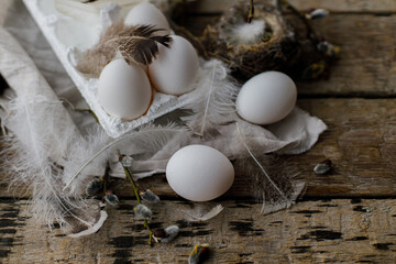 Easter natural eggs in tray, feathers, willow branches, nest, linen cloth on aged wooden table. Stylish Easter rustic still life. Simple rural aesthetics. Happy Easter