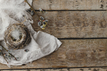 Stylish Easter rustic flat lay. Nest with feathers, willow branches, linen cloth on aged wooden table. Happy Easter! Simple Easter rural still life aesthetics. Space for text