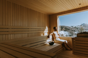 Young man relaxing in the sauna and watching winter forest through the window