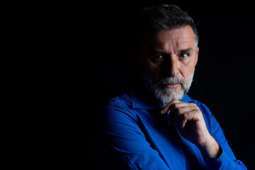 Portrait of an attractive bearded mature man in low key studio background. Portrait of serious senior bearded man on black background. Low key portrait of mature man.