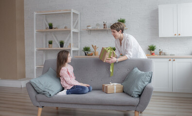 A loving mother gives a gift to her daughter sitting on the sofa in the living room.