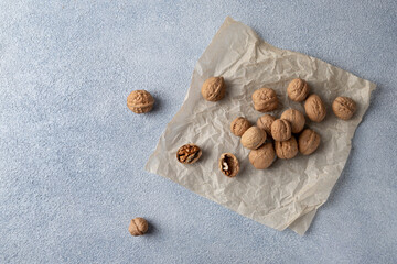Top view of a scattering of walnuts in a shell lying on parchment paper. Blue textured background, copy space, horizontal orientation.