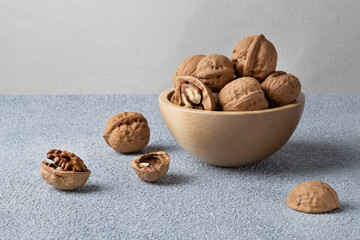 Unpeeled walnuts in a wooden bowl standing on a blue textured background. Horizontal orientation, close-up.