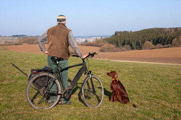 On a glorious spring morning, a cyclist and his Irish Setter dog take a break and enjoy the view of...