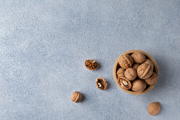 Top view of walnuts lying in a wooden bowl. Horizontal orientation, copy space, blue textured background.