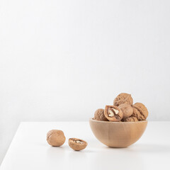A wooden bowl with unpeeled walnuts stands on a white table.