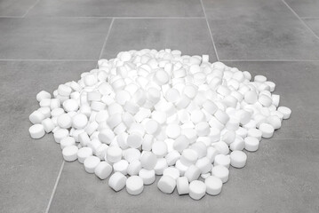 A pile of salt tablets for a water softener lying on ceramic tiles.