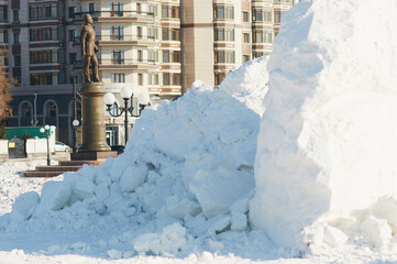A pile of frozen chunks of snow on the sidewalk. Destroyed New Year's ice slide. The monument and residential building in the background. Sunny winter day.