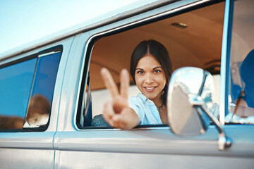 See you on the road. Shot of a young woman leaning out of a vans window and showing a peace sign on a roadtrip.