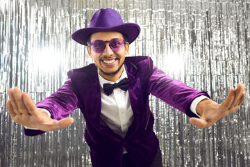 Funny handsome man wearing purple velvet suit, bowtie, glasses and hat having fun at party....