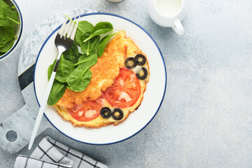 Omelette with tomatoes, black olives, cottage cheese and green spinach herbs on white plate on grey concrete background. Delicious breakfast. Healthy breakfast food. Top view.