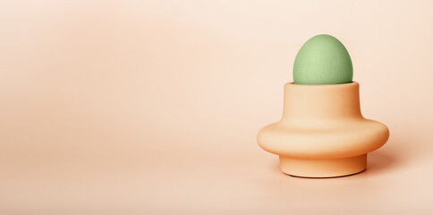 Banner with green dyed Easter egg in cup, server or holder on beige background. Religious holiday symbol. Breakfast food. Space for text. High quality photo