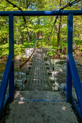 Fototapeta na wymiar Suspension footbridge spans the river with waterfall. Joaveski waterfall. Estonia. Baltic.