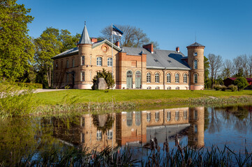 Fototapeta na wymiar Old brick manor house in Lasila. Estonia, Baltic states. Landscape of the estate with reflection in the pond, spring sunny day. Today it is home to Lasila School.