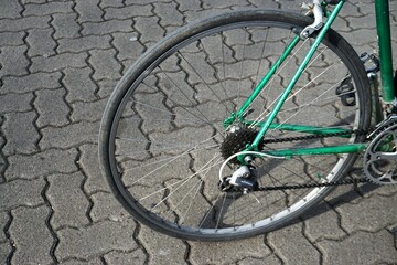 Hinterrad von grünem Rennrad auf grauen Pflastersteinen bei Sonne im Frühling 