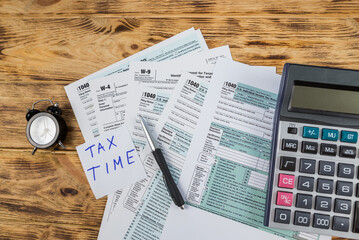 tax forms 1040 with calculator and accessories on wooden background.