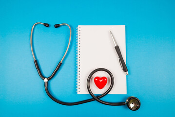 Stethoscope with red heart, notepad and pen on a blue background.