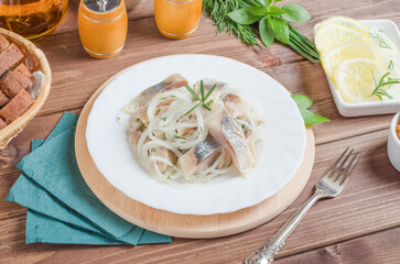 Fresh herring with onion and dill on a white plate on a dark wooden background
