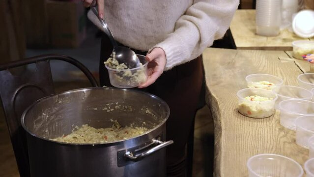 Female hand fills plastic bowls with rice porridge to help homeless people affected by war in ukraine