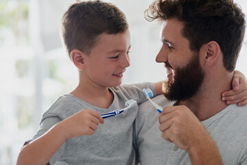 Got to keep the tooth decay at bay. Shot of a father and his little son brushing their teeth...