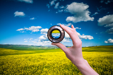 Hand holds lens viewfinder against nature in Tuscany at spring. - 495750188