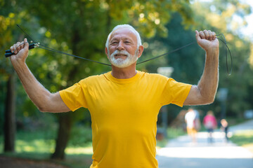 Portrait of senior athlete exercising outside. Senior man holding jump rope