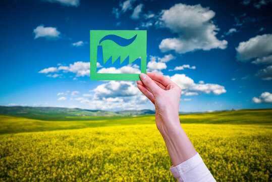 Hand holds green industry symbol on nature background.