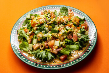 Um prato com salada de vegetais frescos sobre superfície de cor alaranjada.