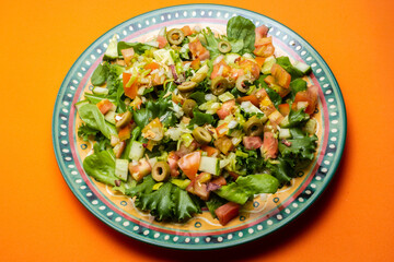 Um prato com salada de vegetais frescos sobre superfície de cor alaranjada.