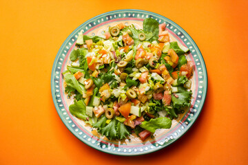 Um prato com salada de vegetais frescos sobre superfície de cor alaranjada.