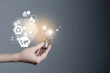 Energy innovation light bulb with future industry of power generation icons graphic interface in woman`s hands. Concept of sustainability development and alternative energy.
