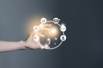 Energy innovation light bulb with future industry of power generation icons graphic interface in woman`s hands. Concept of sustainability development and alternative energy.