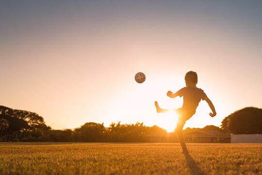 Silhouette of child boy playing football kicking ball