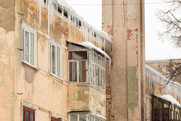 Large ice icicles hang from the edge of the roof. Against the background of the wall of an old brick house. Large cascades, even beautiful rows. Cloudy winter day, soft light.
