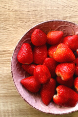 Pink bowl full of fresh strawberries on wooden table. Flat lay.