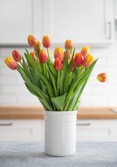 A beautiful bouquet of red and yellow tulips in a white vase on a blue wooden countertop against a white kitchen background. Spring time concept