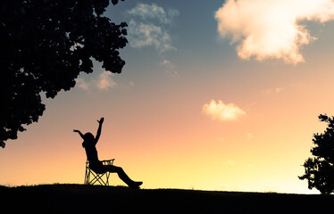 Happy woman sitting outdoors looking up to the sky with arms outstretched. People freedom and happiness concept.	