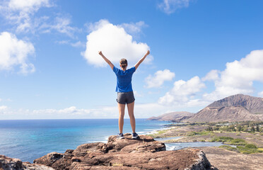 Happy woman on a mountain looking up to the blue sky with arms up. Active healthy lifestyle concept. 