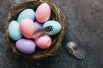 Happy Easter concept. Preparation for holiday. Colorful pastel decorated easter eggs in nest on grunge scratched dark black shale background. Simple minimalism flat lay top view copy space