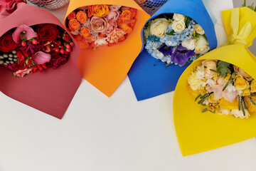 4 bouquets of flowers in multi-colored packages lie on the surface next to each other. bouquets of red, orange, blue and yellow flowers