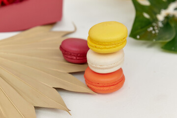 macaroons of different colors lie on top of each other on a white background with green leaves