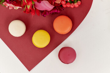 macaroon cakes of yellow, white, orange and burgundy colors lie on a background with flowers. still-life