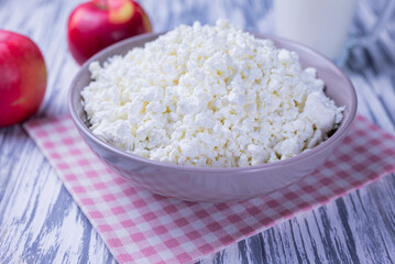 dairy product cottage cheese in a plate with a glass of milk and apples on a wooden background