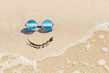 Fototapeta na wymiar A painted smile on the sand and sunglasses with the flag of the Honduras. The concept of a positive and successful holiday in the resort of the Honduras.
