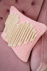 Fototapeta na wymiar Knitted handmade pillow with pink threads lies on the sofa.
