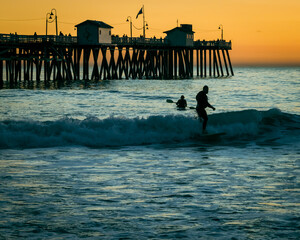 Silhouette of two people surfing at the beautiful seashore of San Clemente - obrazy, fototapety, plakaty