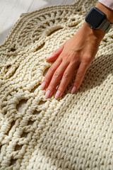 Women's hands lie on a plaid of coarse knitted wool on a wooden floor, top view. Handmade carpet