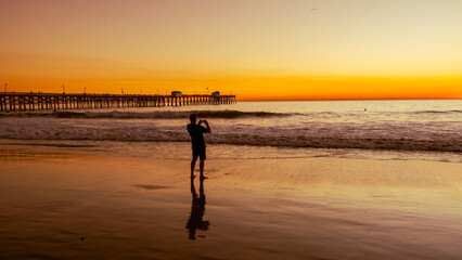 Silhouette of a guy taking a landscape picture of the san clement seashore sunset - obrazy, fototapety, plakaty