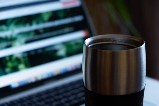 metal thermo mug with a hot drink on the background of a laptop