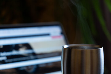 metal thermo mug with a hot drink on the background of a laptop